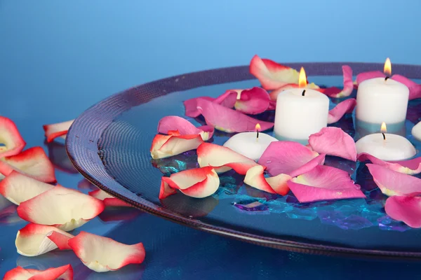 Pétales de roses et bougies dans l'eau en vase sur fond bleu close-up — Photo