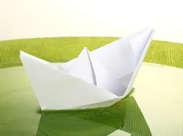 Color paper ship in water on green plate, close-up — Stock Photo, Image