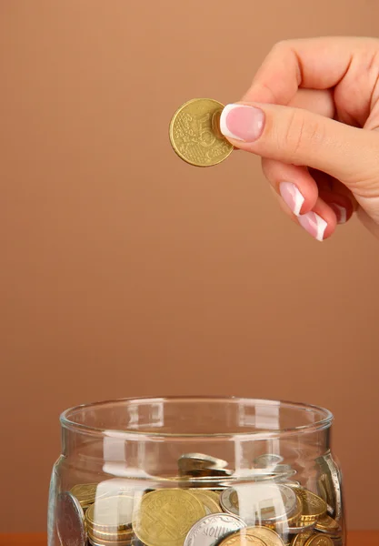 Risparmio, mano femminile mettendo una moneta in bottiglia di vetro, su sfondo di colore — Foto Stock