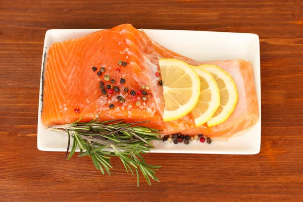 Fresh salmon fillet with herbals and lemon slices on plate,on wooden background — Stock Photo, Image