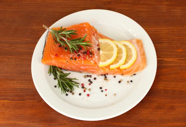 Filet de saumon frais avec des herbes et des tranches de citron sur assiette, sur fond de bois — Photo