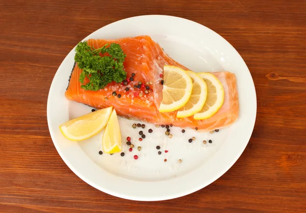 Fresh salmon fillet with herbals and lemon slices on plate,on wooden background — Stock Photo, Image