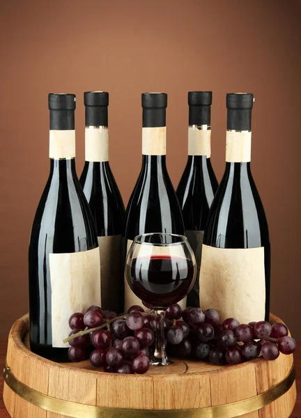 Composition of wine bottles, glasses and grape,on wooden barrel, on brown background — Stock Photo, Image