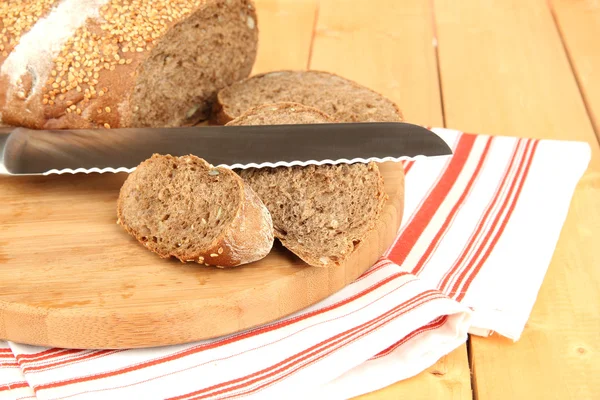 Pane affettato con semi di sesamo e coltello sul tagliere sul tavolo di legno da vicino — Foto Stock