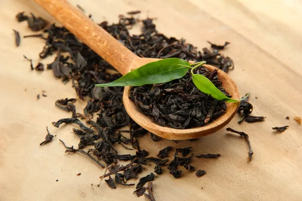 Trockener Tee mit grünen Blättern in Holzlöffel, auf Holzgrund — Stockfoto