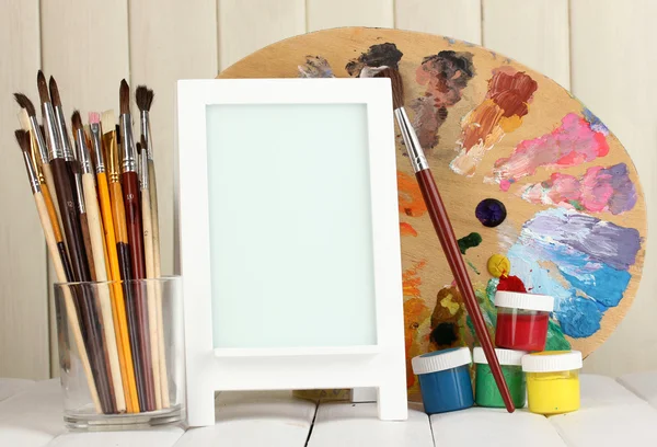 Photo frame as easel with artist's tools on wooden background — Stock Photo, Image