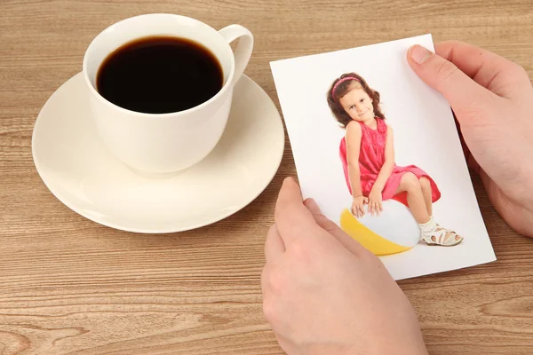 Photo in hands and cup of coffee on wooden table — Stock Photo, Image