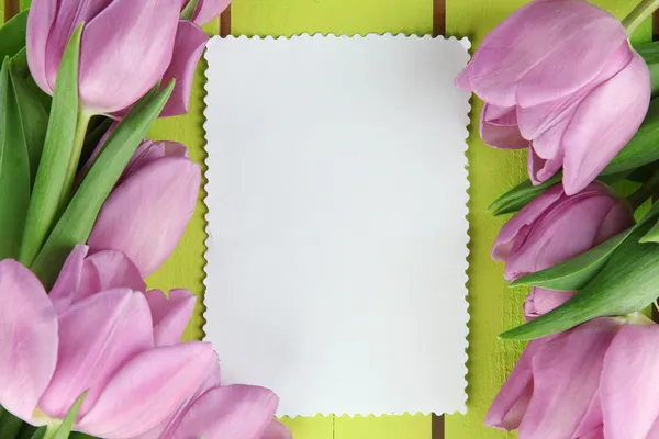 Hermoso ramo de tulipanes morados y tarjeta en blanco sobre fondo de madera verde —  Fotos de Stock