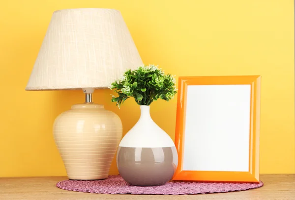 Marco de fotos colorido, lámpara y flores en la mesa de madera sobre fondo amarillo — Foto de Stock