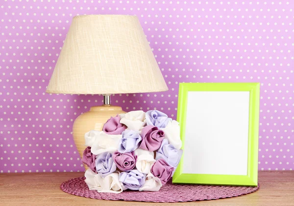 Cornice fotografica colorata, lampada e fiori su tavolo in legno su sfondo a pois lilla — Foto Stock