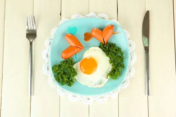 Sausages in form of hearts, scrambled eggs and parsley, on color plate, on wooden background — Stock Photo, Image