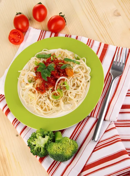 Smakfull spagetti med saus og grønnsaker på tallerkenen på trebord. – stockfoto