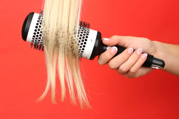 Blond curls brushing comb on color background — Stock Photo, Image