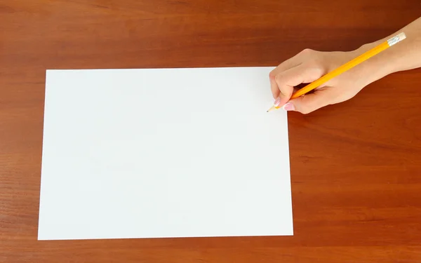 Рука с карандашом на белой бумаге, на деревянном фоне — стоковое фото