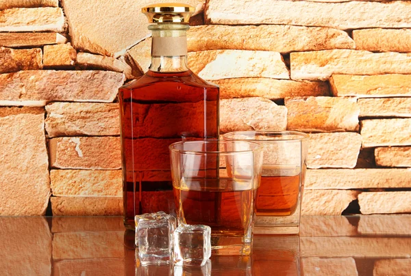 Бутылки и стаканы виски и льда на фоне кирпичной стены — стоковое фото