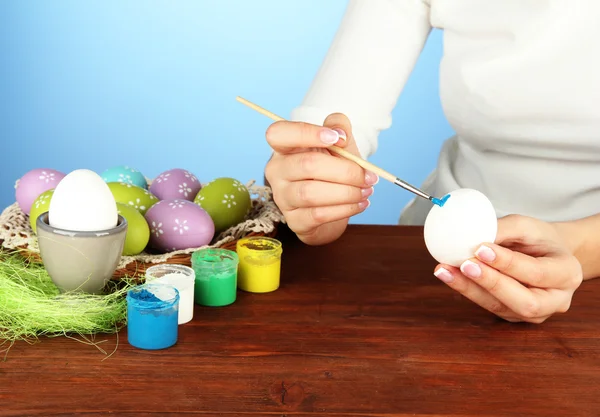 Jovem mulher pintando ovos de Páscoa, no fundo de cor — Fotografia de Stock