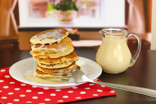 Frittelle dolci su piatto con latte condensato sul tavolo in camera — Foto Stock