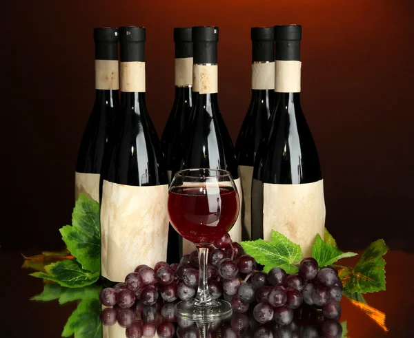 Composition of wine bottles, glass and grape, on dark red background — Stock Photo, Image