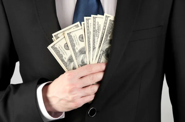 Business man hiding money in pocket on grey background — Stock Photo, Image