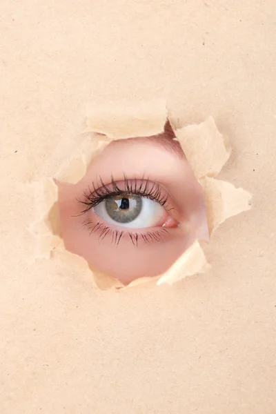 Female eye looking through hole in sheet of paper — Stock Photo, Image