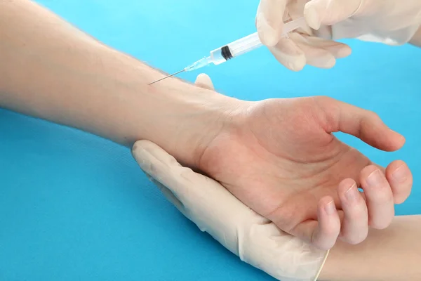 Läkare anläggning spruta med vaccin i patientens hand, på blå bakgrund — Stockfoto