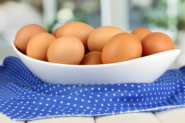 Яйца в белой миске на деревянном столе на фоне окна — стоковое фото