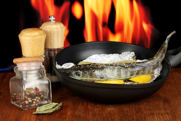 Ryby v pánvi s bylinkami a citronem na palubě na dřevěný stůl na ohni pozadí — Stock fotografie