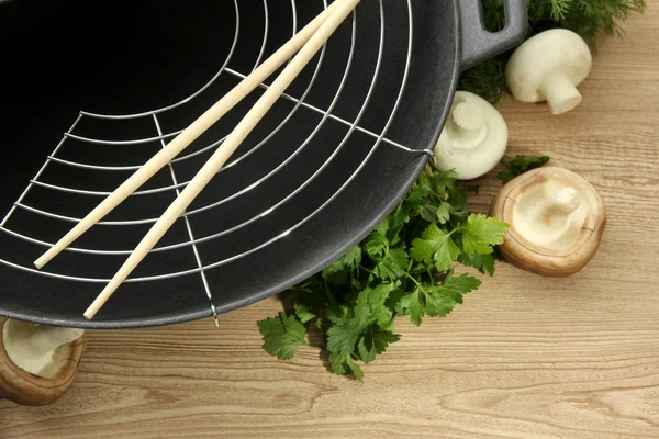 Black wok pan and vegetables on kitchen wooden table, close up