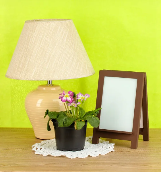 Moldura de foto marrom e lâmpada na mesa de madeira no fundo da parede verde — Fotografia de Stock
