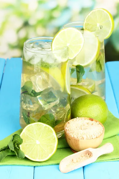 Bicchieri di cocktail con lime e menta su tavolo di legno blu su sfondo brillante — Foto Stock