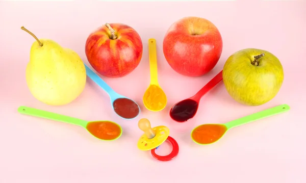 Puré de bebé en cucharas con pezón y frutas sobre fondo rosa — Foto de Stock