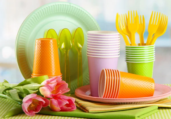 Multicolored plastic tableware on table with tulips close up — Stock Photo, Image