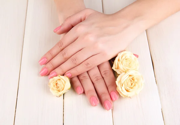 Mains de femme avec manucure rose et fleurs, sur fond bois — Photo
