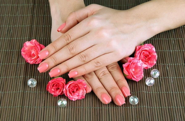 Mani donna con manicure rosa e fiori, su sfondo tappetino di bambù — Foto Stock