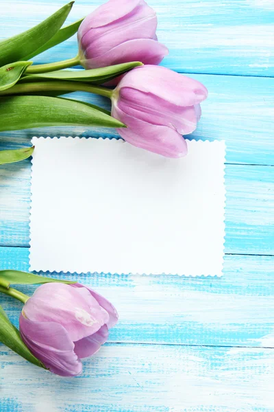 Beautiful bouquet of purple tulips and blank card on blue wooden background Royalty Free Stock Images