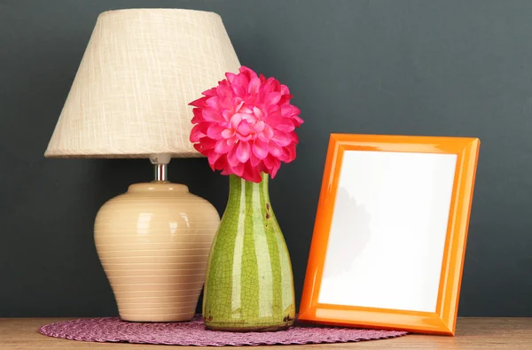 Colorful photo frame, lamp and flowers on wooden table on grey background — Stock Photo, Image