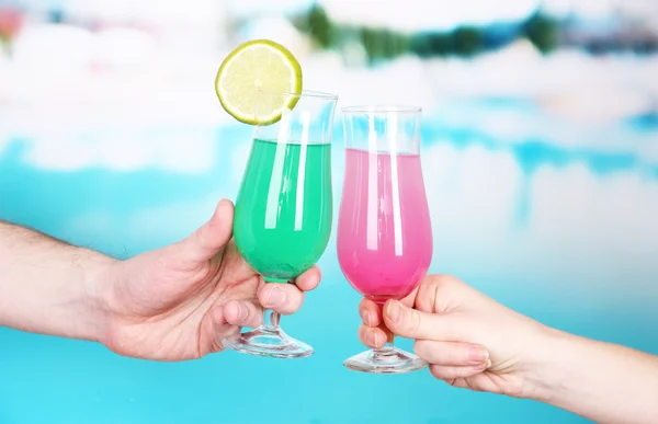 Cocktails in men's and women's hands on pool background — Stock Photo, Image