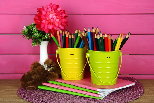 Lápis coloridos em pails com copybooks e urso na mesa sobre fundo rosa — Fotografia de Stock