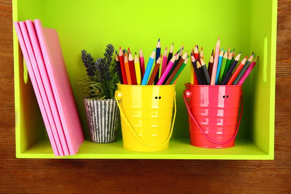 Crayons colorés dans des seaux sur étagère avec des copybooks sur fond en bois — Photo