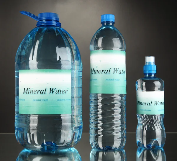 Different water bottles with label on grey background — Stock Photo, Image