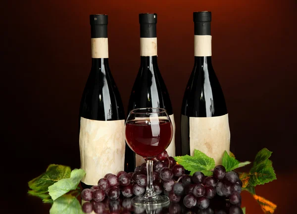 Склад пляшок вина, скла і винограду на темно-червоному тлі — стокове фото