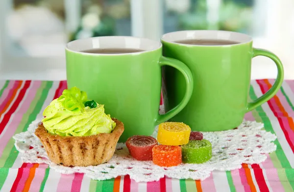 Cups of tea with cake and candy on table in room — Stock Photo, Image
