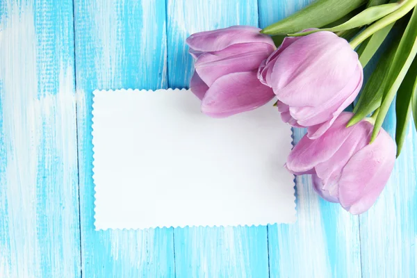 Hermoso ramo de tulipanes morados y tarjeta en blanco sobre fondo de madera azul —  Fotos de Stock