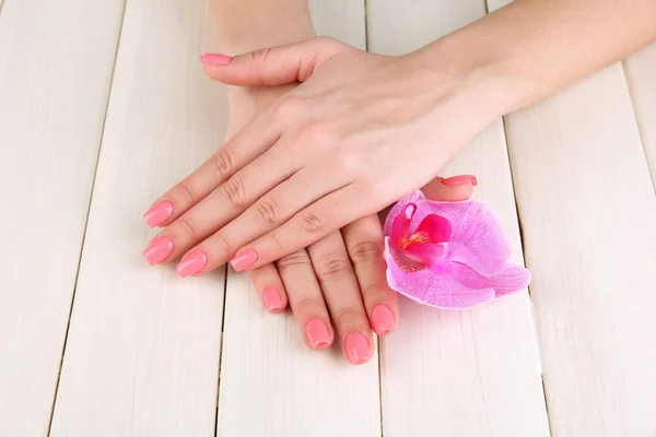 Женские руки с розовым маникюром и орхидеей на деревянном фоне — стоковое фото