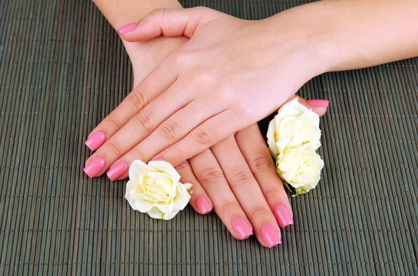 Manos de mujer con manicura rosa y flores, sobre fondo de estera de bambú — Foto de Stock