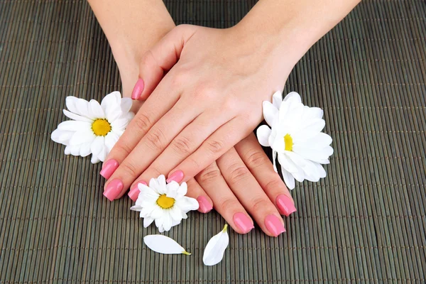 Mani donna con manicure rosa e fiori, su sfondo tappetino di bambù — Foto Stock