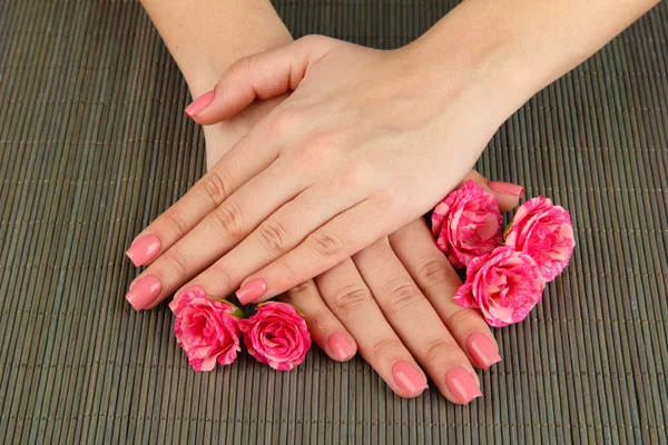 Mãos de mulher com manicure rosa e flores, em fundo tapete de bambu — Fotografia de Stock