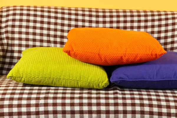 Colorful pillows on couch on yellow background — Stock Photo, Image