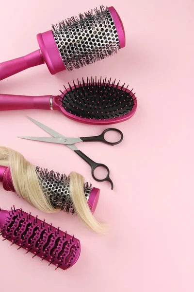 Comb brushes, hair and cutting shears, on pink background — Stock Photo, Image