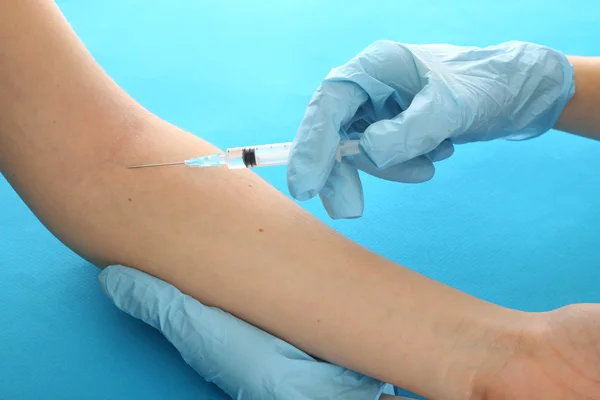 Médico sosteniendo la jeringa con una vacuna en la mano del paciente, sobre fondo azul — Foto de Stock